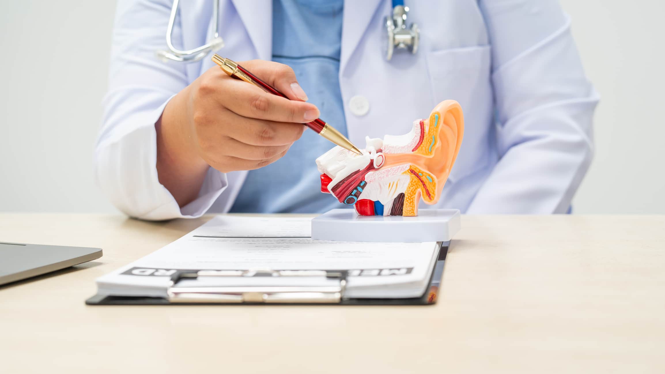 A female doctor sits at a table in a hospital, discussing hearing loss, tinnitus, and balance problems like dizziness and vertigo, addressing issues such as ear infections and inner ear degeneration.